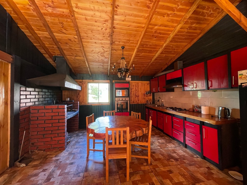 Comedor y cocina con mesa larga y chimenea de piedra en Sendas del Volcán, Licán Ray